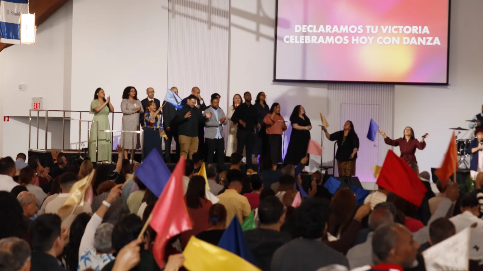 The congregation worships with colorful flags while the worship team sings on the platform